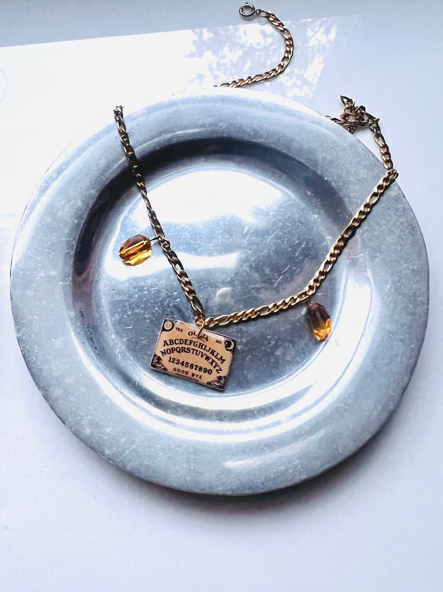 Ouija board charm on a gold chain necklace with two vintage orange faceted gem beads.